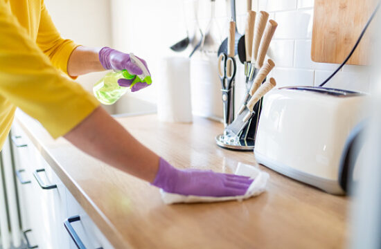 Hands in gloves disinfecting kitchen counter and wiping with paper towel against viruses