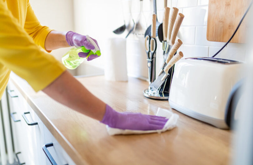 Hands in gloves disinfecting kitchen counter and wiping with paper towel against viruses