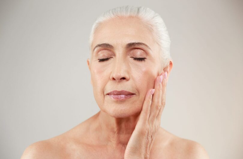 Picture of an amazing serious naked elderly woman posing isolated over grey background. Eyes closed.